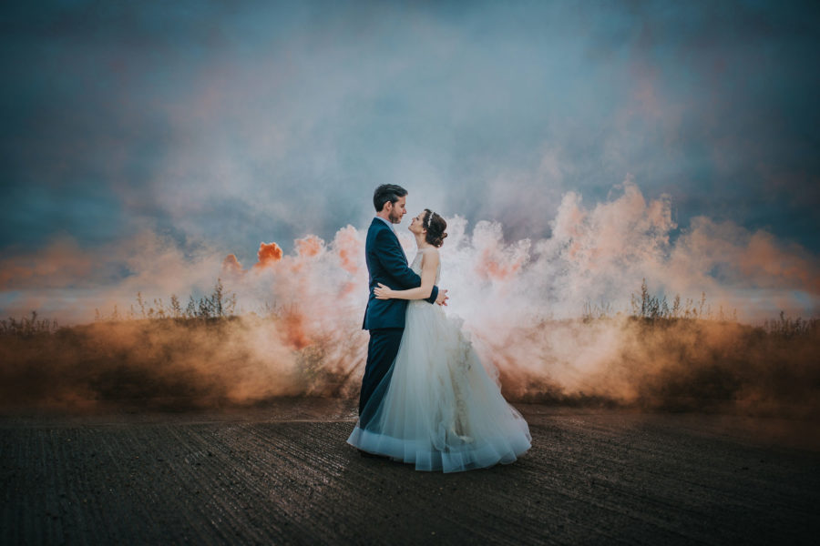 Bride and groom embrace in front of a smoke bomb